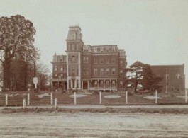 Historic photograph of a large, multi-story brick institutional building with a central tower, identified as St. Louis’s Social Evil Hospital. A fence and open grounds surround the building, with trees visible on either side.